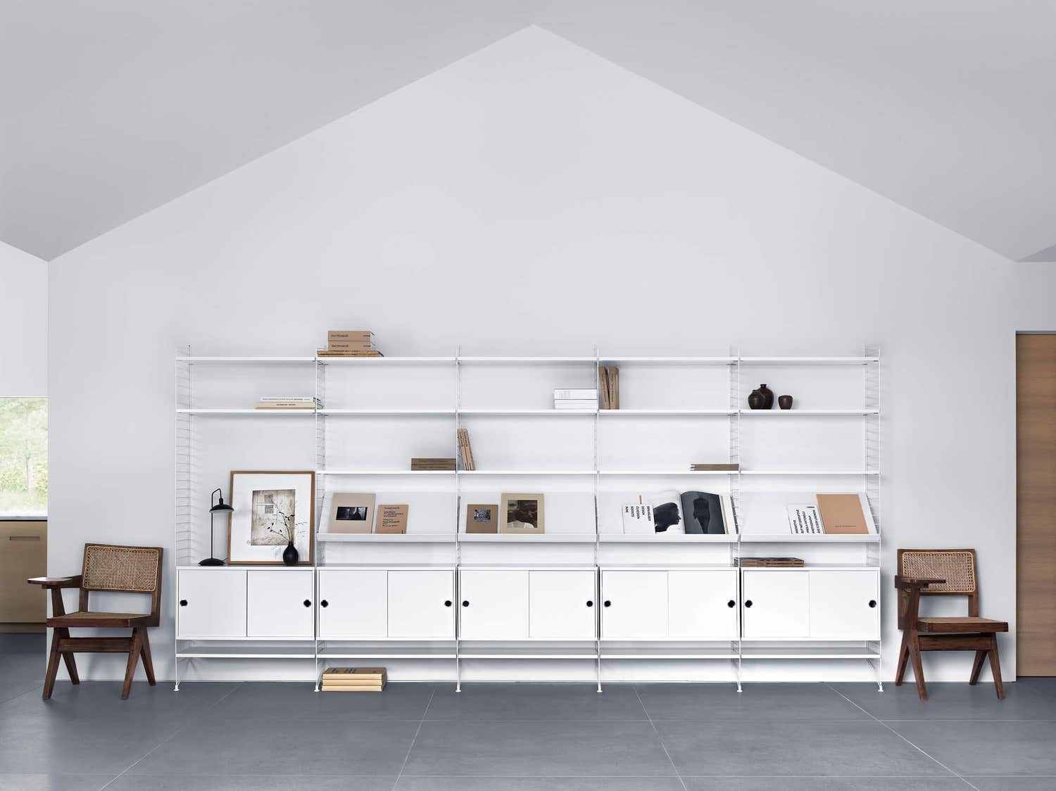 Wei&szlig;es String-Regal im Wohnzimmer, bestehend aus wei&szlig;en Schr&auml;nken mit Schiebet&uuml;ren, wei&szlig;en Regalb&ouml;den und dazugeh&ouml;riger inspirierender Einrichtung.
